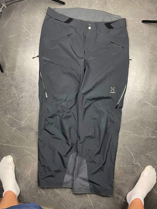 Haglöfs black softshell outdoor trousers with zipped pockets and adjustable Velcro waist tabs.