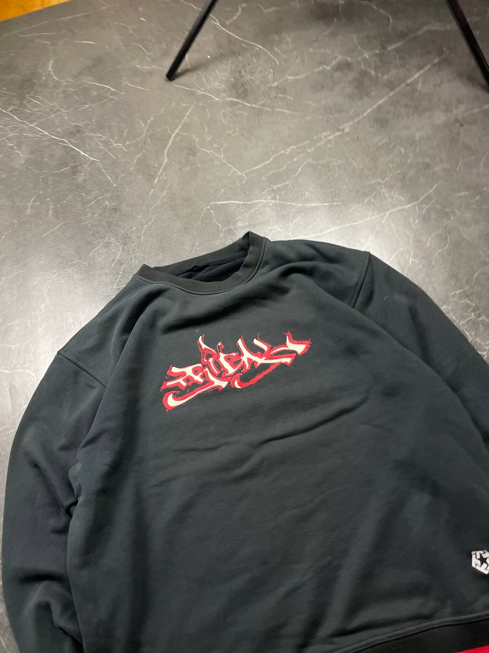 Vintage black crewneck sweatshirt with red and white embroidered logo and striped hem.