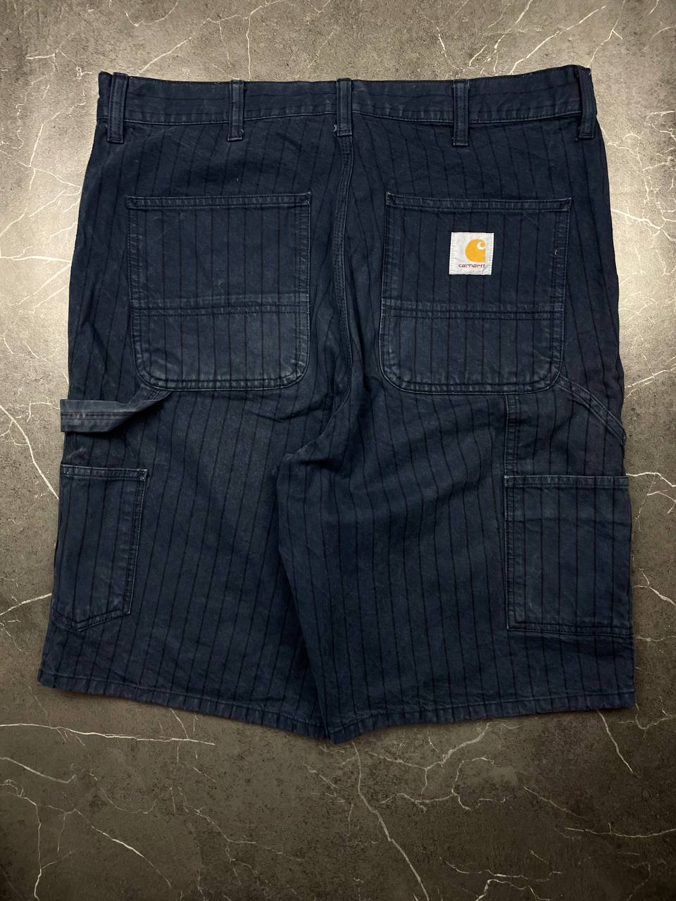 Carhartt navy shorts with pinstripe pattern, utility pockets, and branded metal button.