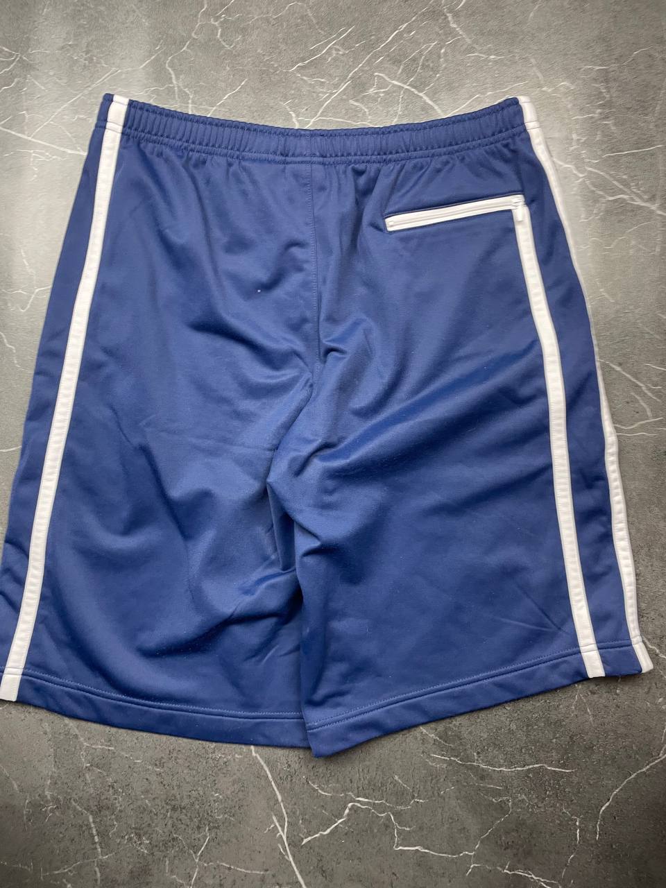 Nike blue sports shorts with white side stripes and small swoosh logo, zip pocket.