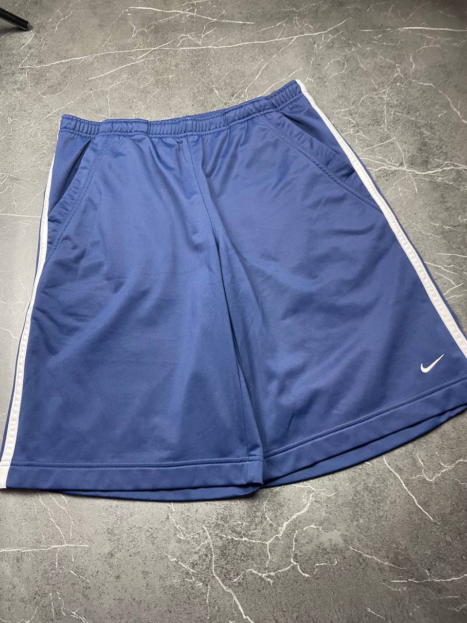 Nike blue sports shorts with white side stripes and small swoosh logo, zip pocket.