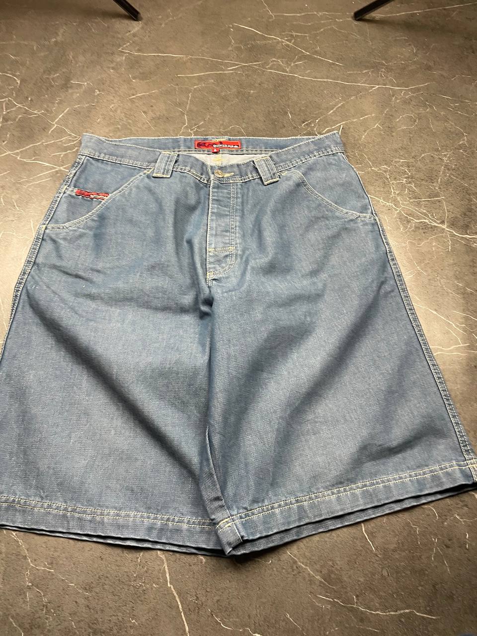 Quiksilver blue denim shorts with yellow contrast stitching and red logo patch.
