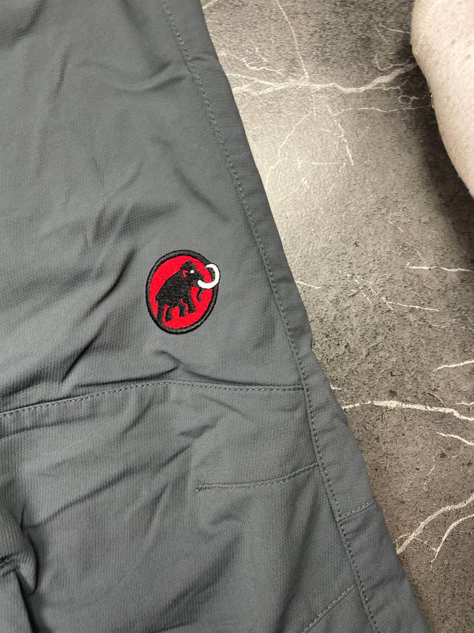 Mammut grey softshell outdoor trousers with reinforced knees, elastic waistband, and zipped pockets.