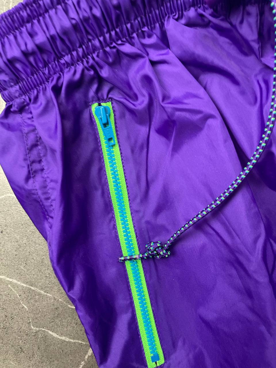 Nike track pants purple with blue and green accents, nylon material, elastic waistband.