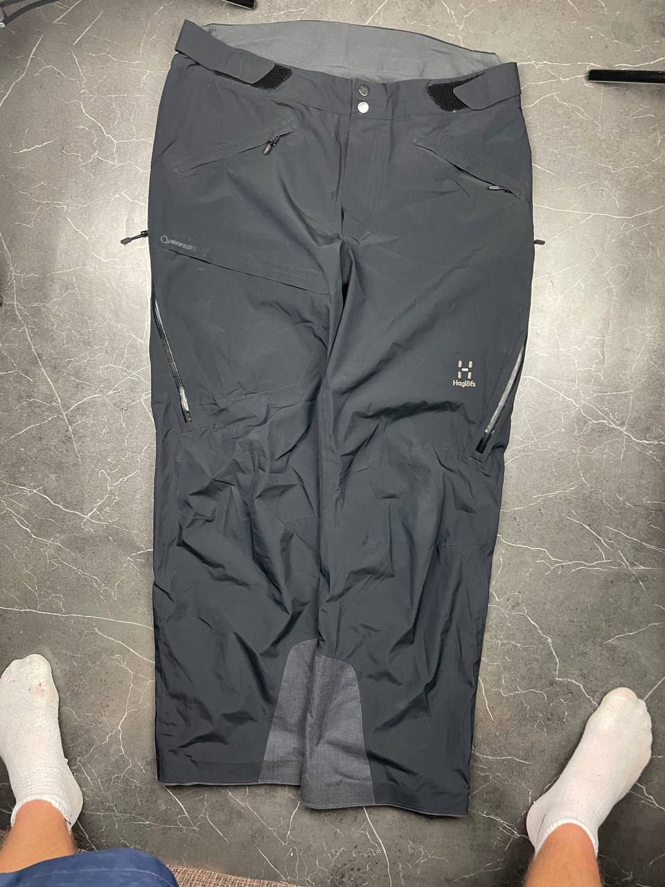 Haglöfs black softshell outdoor trousers with zipped pockets and adjustable Velcro waist tabs.
