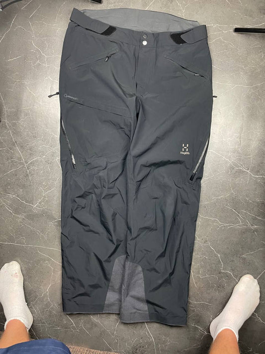Haglöfs black softshell outdoor trousers with zipped pockets and adjustable Velcro waist tabs.