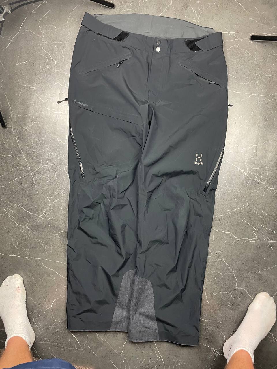 Haglöfs black softshell outdoor trousers with zipped pockets and adjustable Velcro waist tabs.