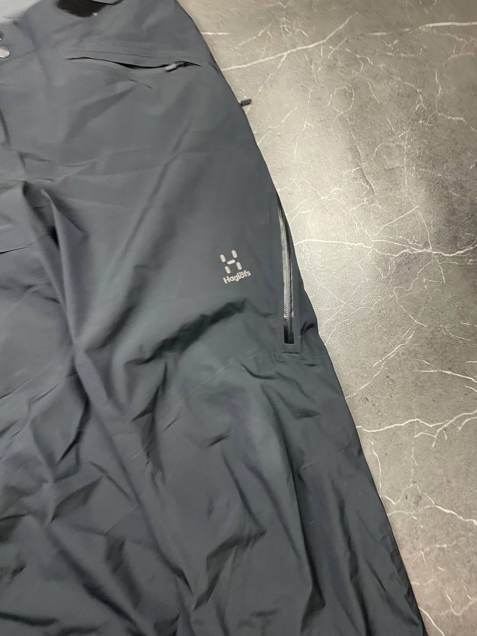Haglöfs black softshell outdoor trousers with zipped pockets and adjustable Velcro waist tabs.