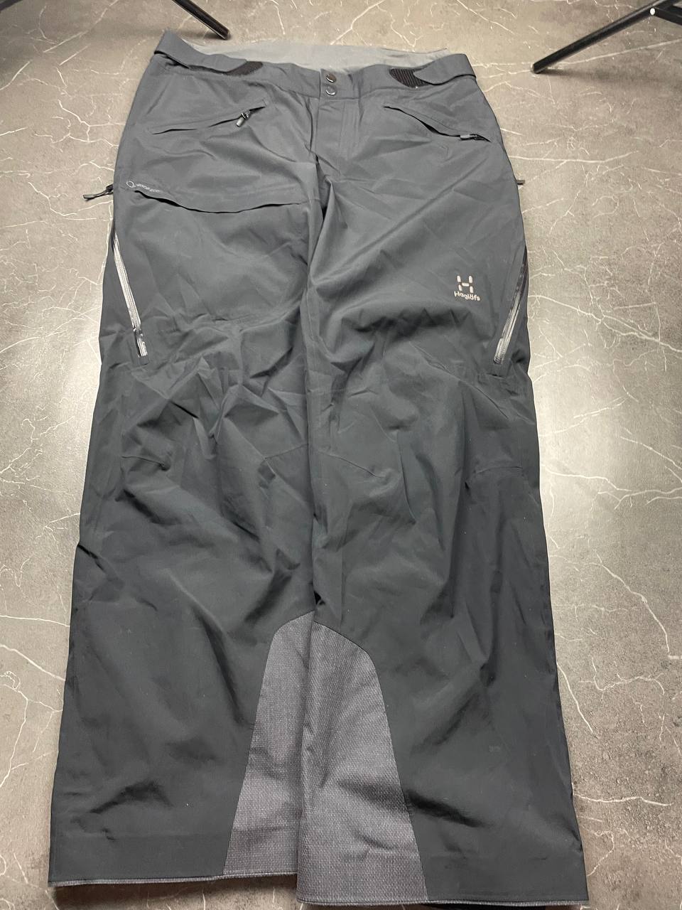 Haglöfs black softshell outdoor trousers with zipped pockets and adjustable Velcro waist tabs.