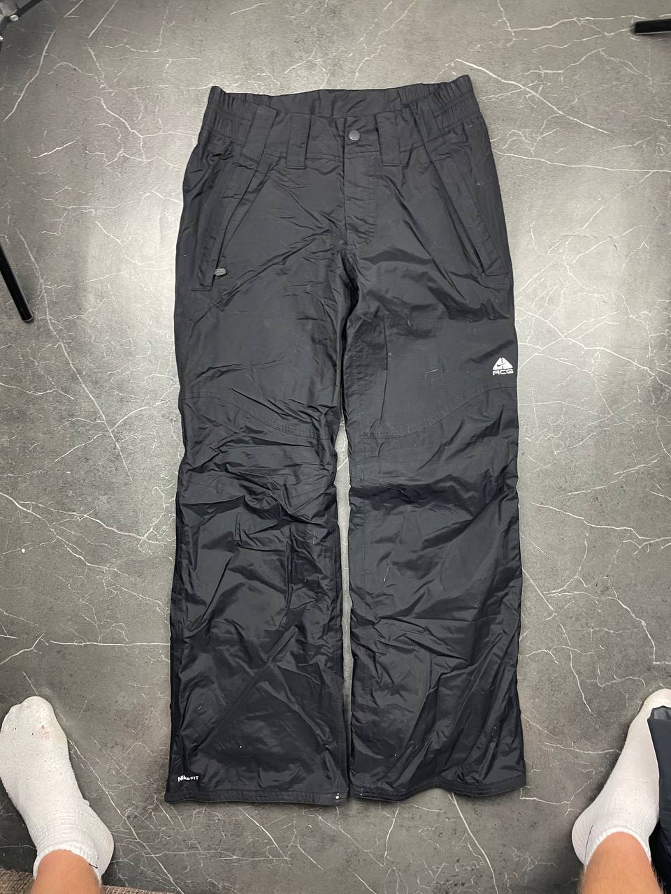 Nike black ski trousers with ACG branding, button closure, and elasticated waistband.