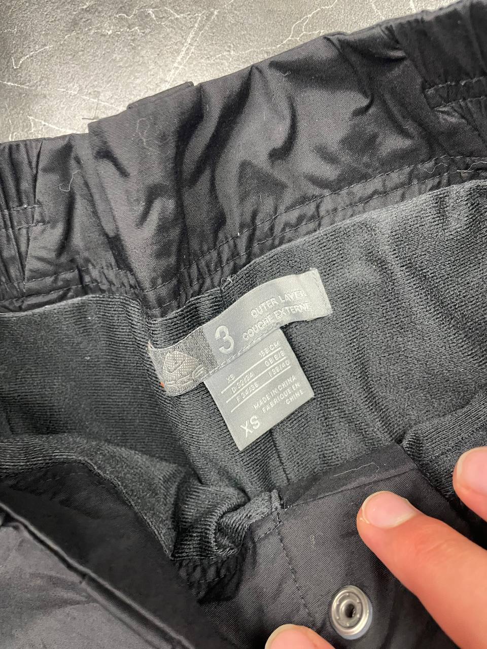 Nike black ski trousers with ACG branding, button closure, and elasticated waistband.
