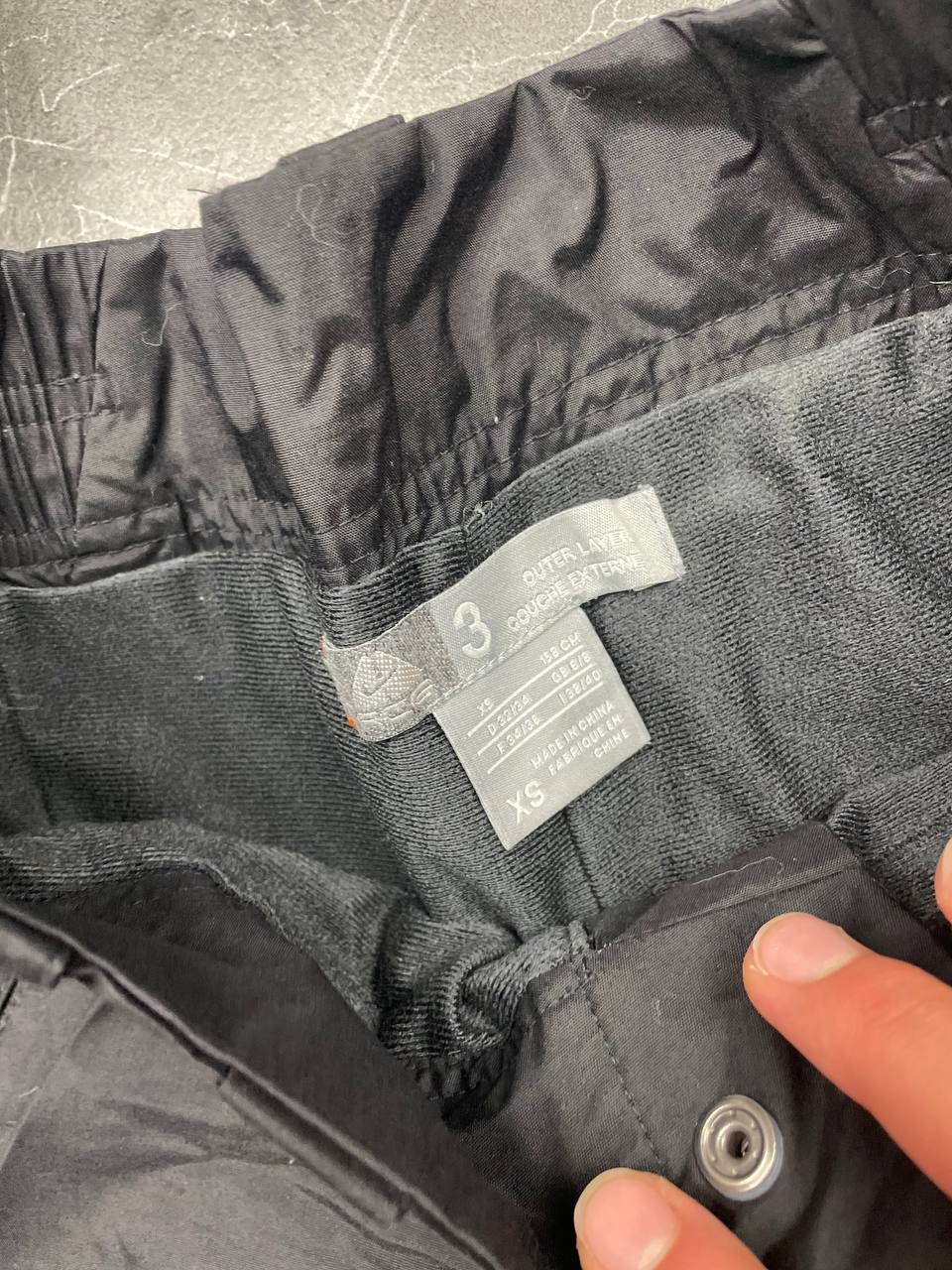 Nike black ski trousers with ACG branding, button closure, and elasticated waistband.