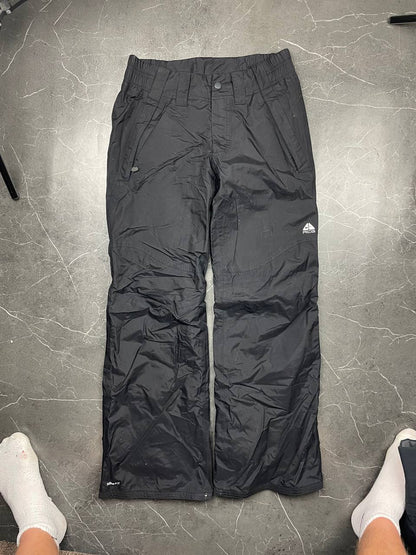 Nike black ski trousers with ACG branding, button closure, and elasticated waistband.