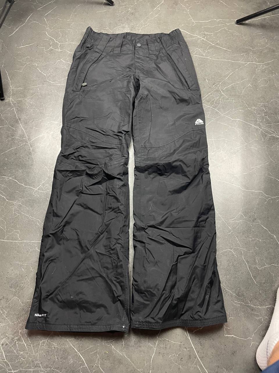 Nike black ski trousers with ACG branding, button closure, and elasticated waistband.
