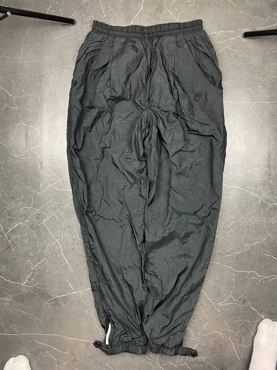 Nike black track pants with elastic waistband, side pockets, and ankle snaps.
