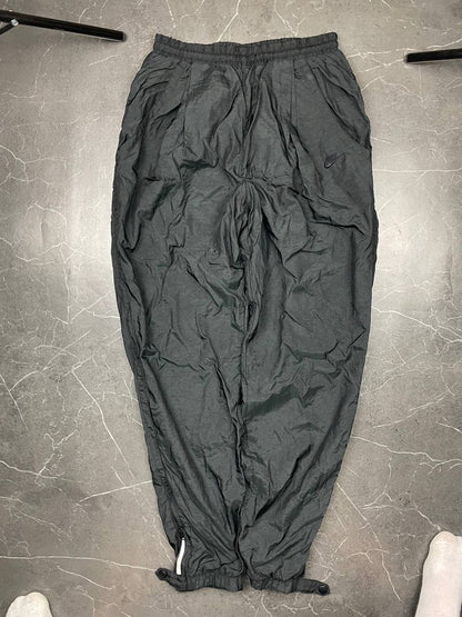 Nike black track pants with elastic waistband, side pockets, and ankle snaps.