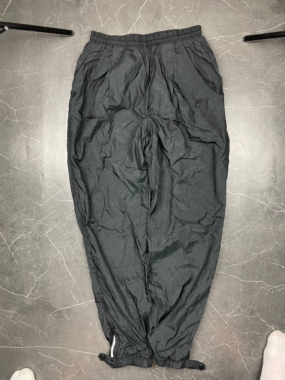 Nike black track pants with elastic waistband, side pockets, and ankle snaps.