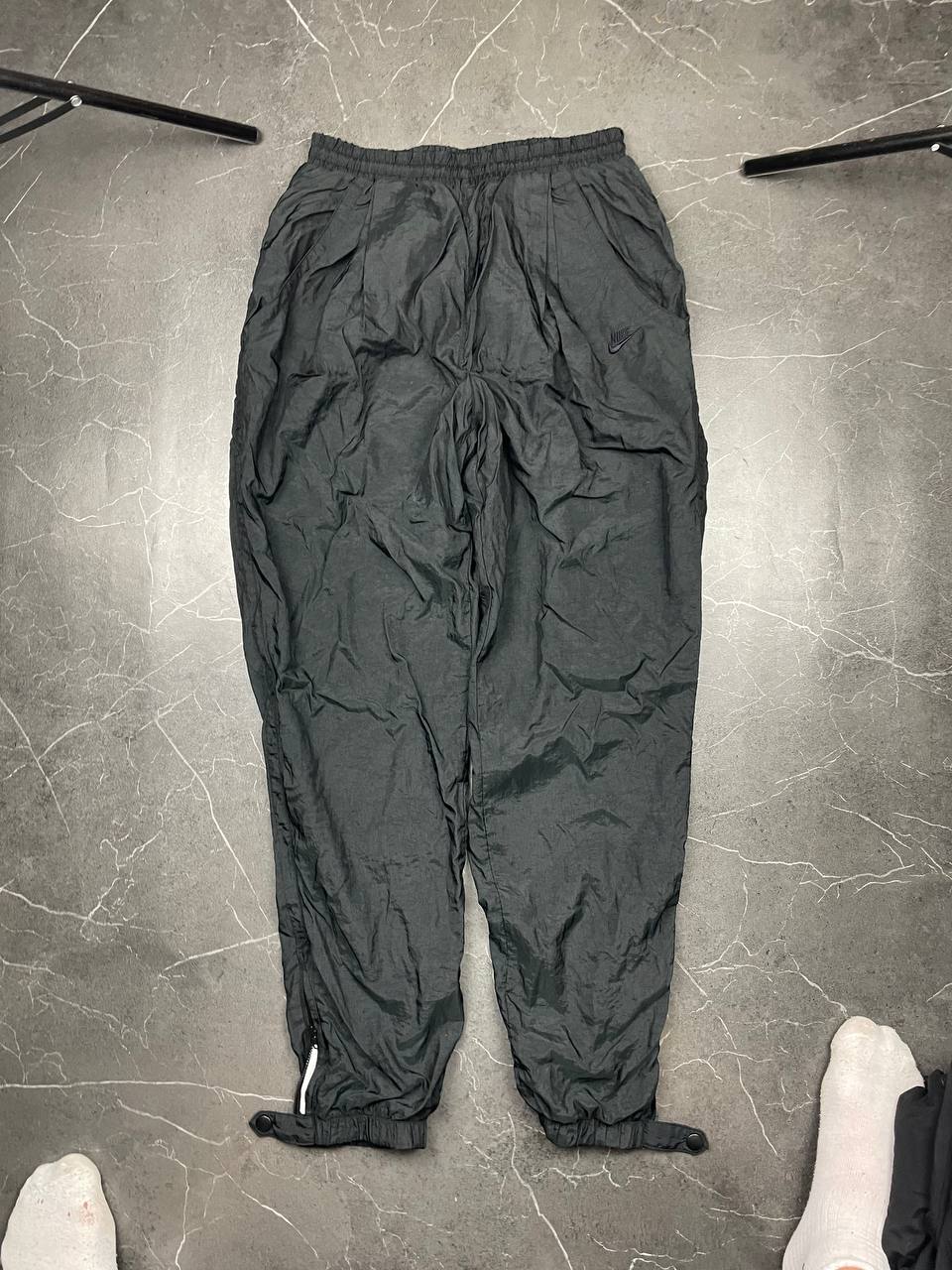 Nike black track pants with elastic waistband, side pockets, and ankle snaps.