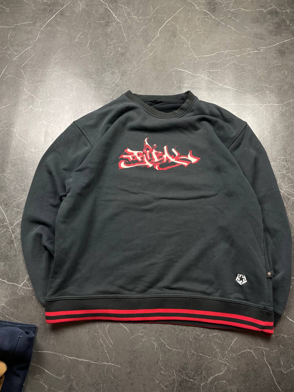 Vintage black crewneck sweatshirt with red and white embroidered logo and striped hem.