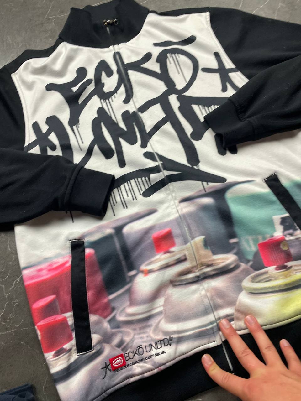 Ecko Unltd black zip-up jacket with graffiti print and spray paint can details.