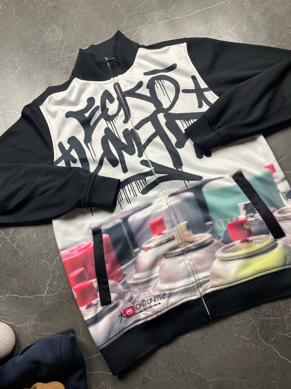 Ecko Unltd black zip-up jacket with graffiti print and spray paint can details.