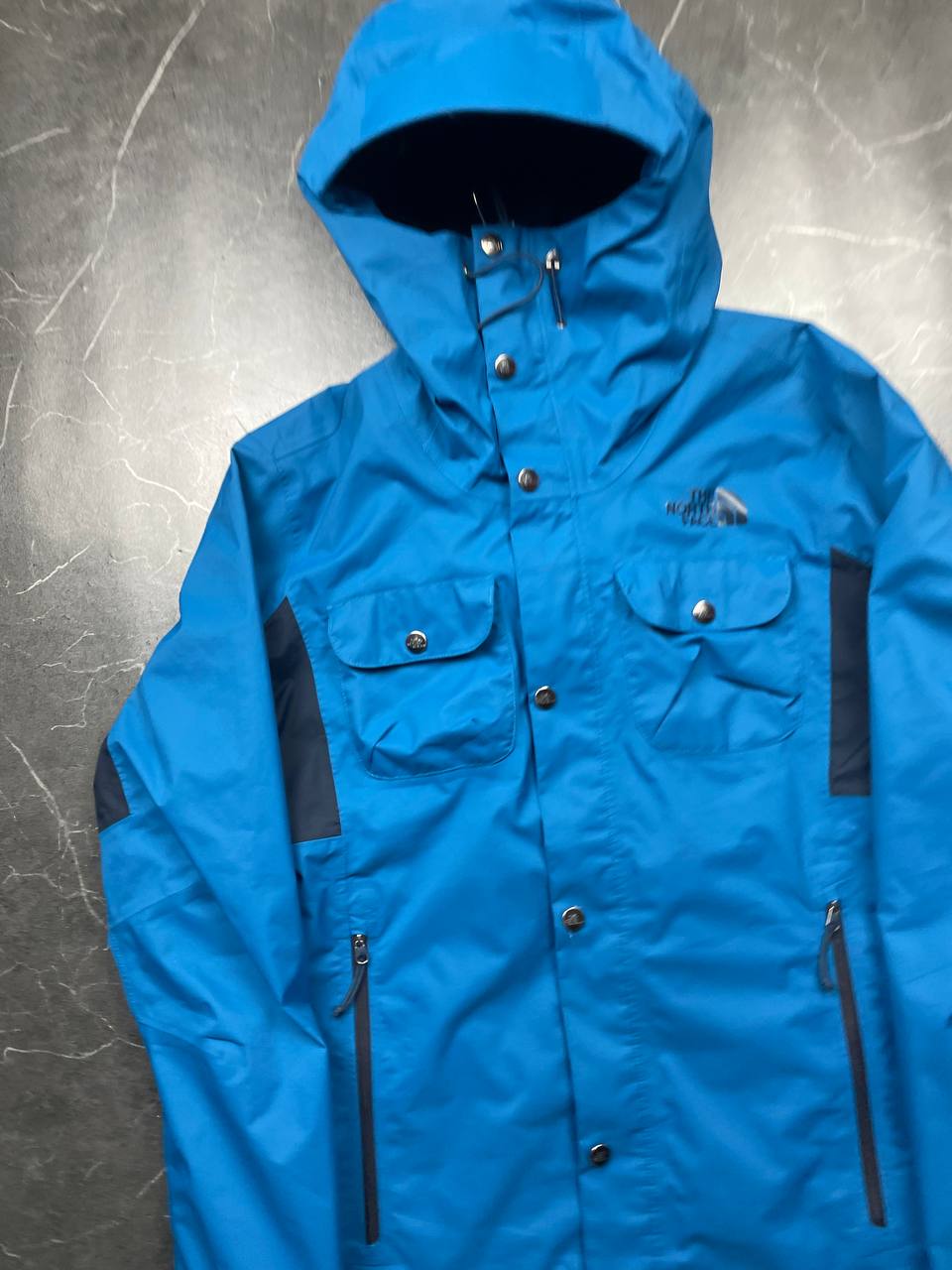 The North Face blue waterproof jacket with black accent panels and adjustable hood.
