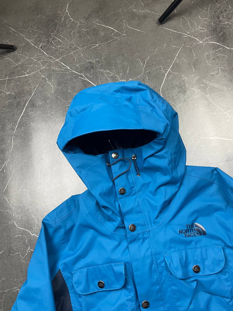 The North Face blue waterproof jacket with black accent panels and adjustable hood.