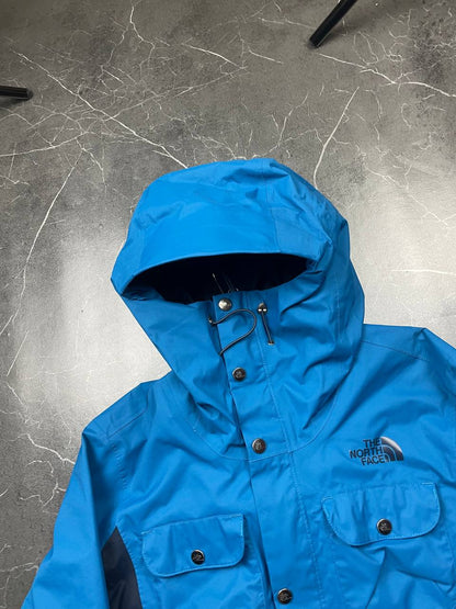 The North Face blue waterproof jacket with black accent panels and adjustable hood.