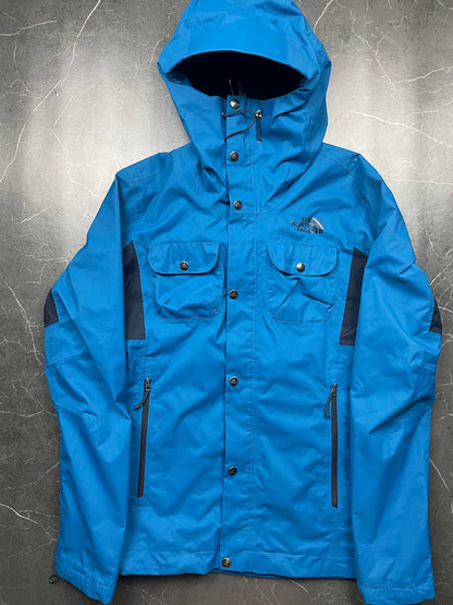The North Face blue waterproof jacket with black accent panels and adjustable hood.