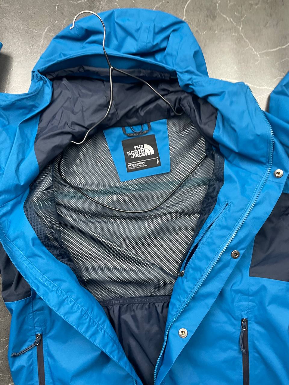 The North Face blue waterproof jacket with black accent panels and adjustable hood.