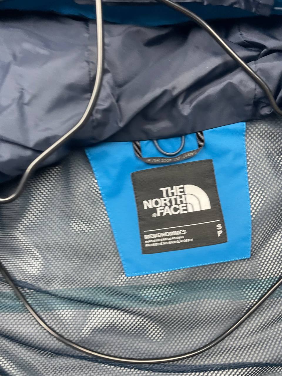The North Face blue waterproof jacket with black accent panels and adjustable hood.