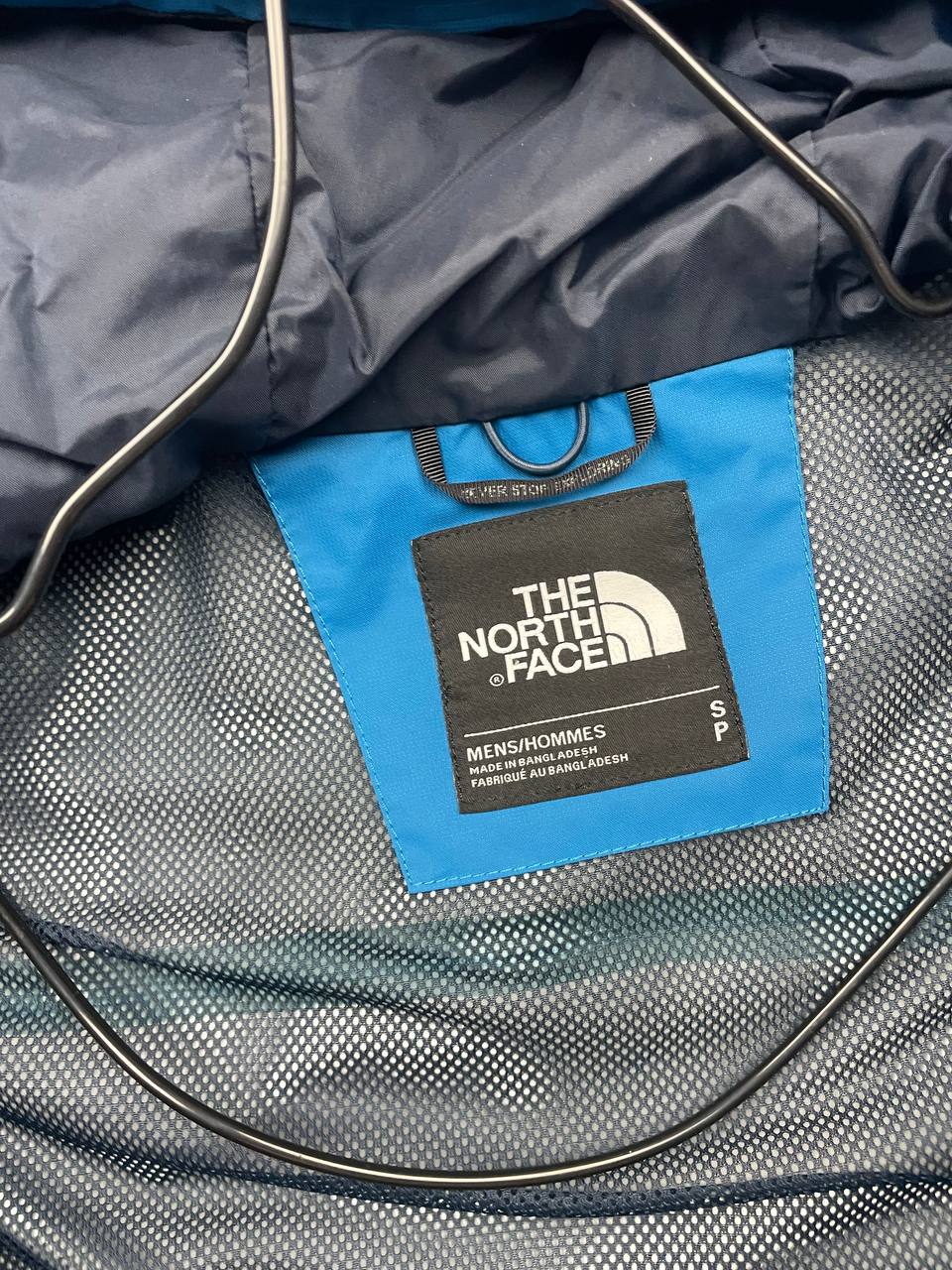 The North Face blue waterproof jacket with black accent panels and adjustable hood.