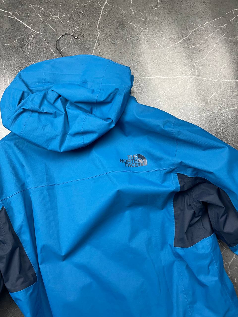 The North Face blue waterproof jacket with black accent panels and adjustable hood.