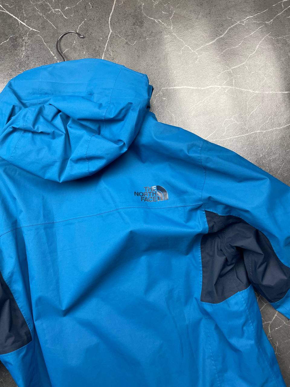 The North Face blue waterproof jacket with black accent panels and adjustable hood.