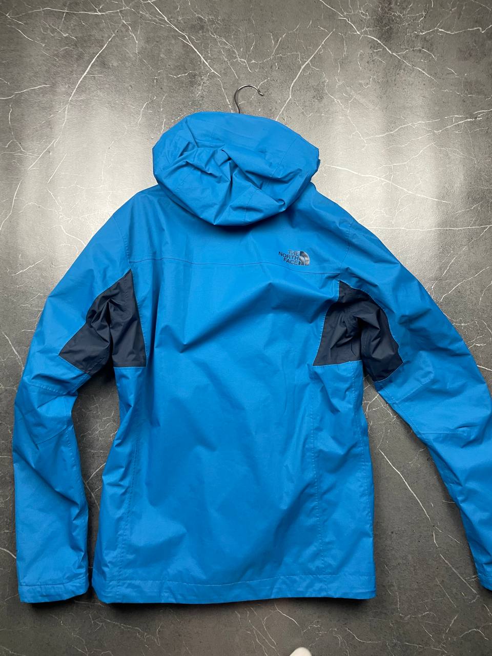 The North Face blue waterproof jacket with black accent panels and adjustable hood.