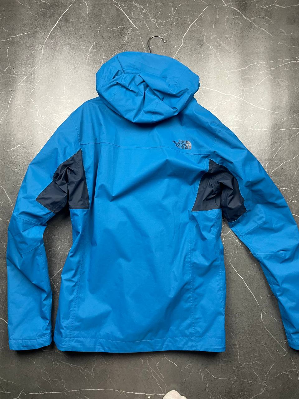 The North Face blue waterproof jacket with black accent panels and adjustable hood.