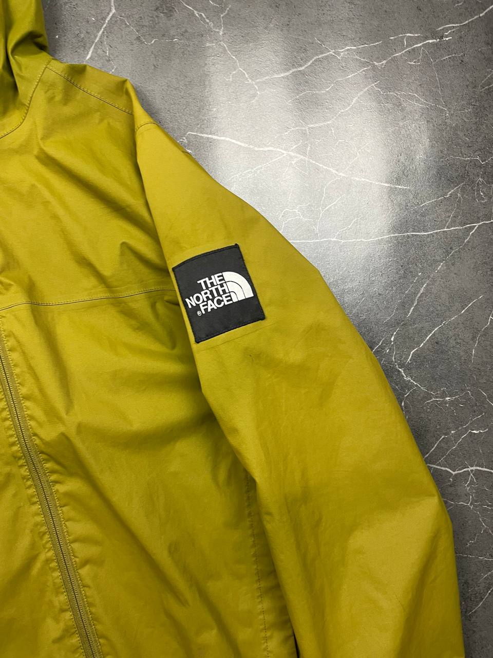 The North Face green hooded windbreaker jacket with branded patch and full zip front.