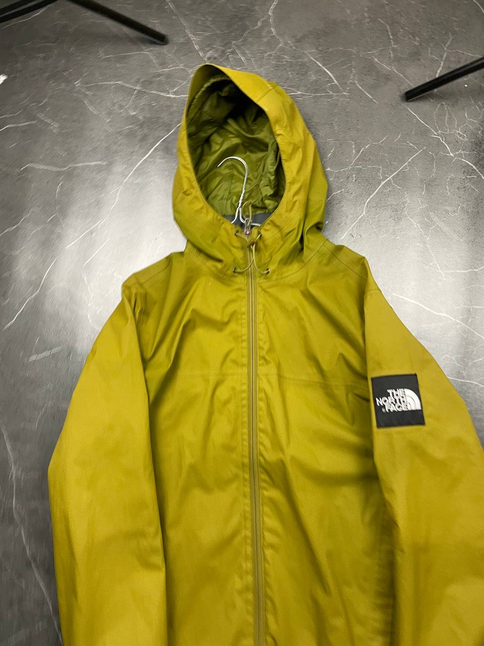 The North Face green hooded windbreaker jacket with branded patch and full zip front.