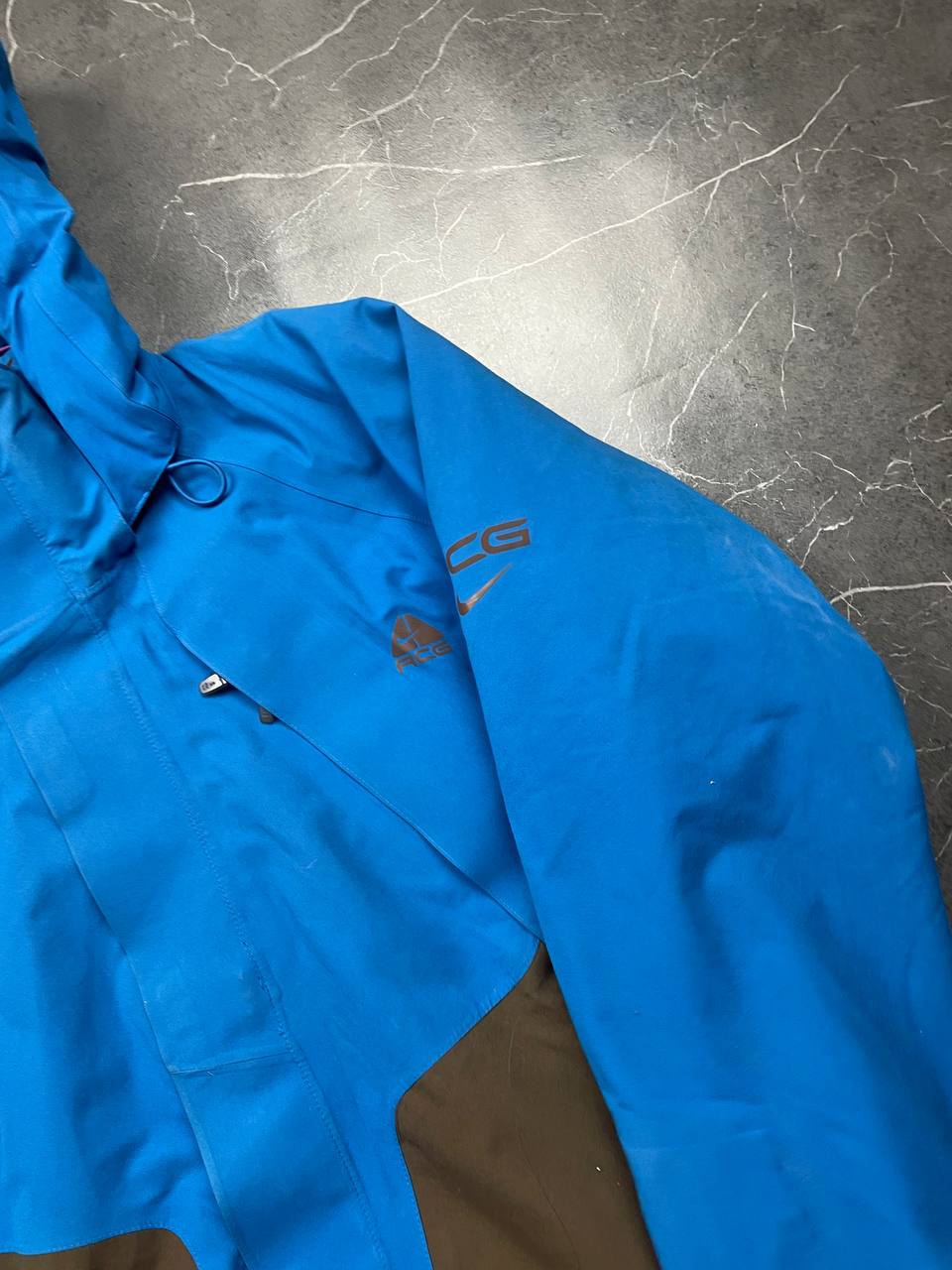 Nike ACG blue and brown waterproof jacket with Gore-Tex label and adjustable hood.
