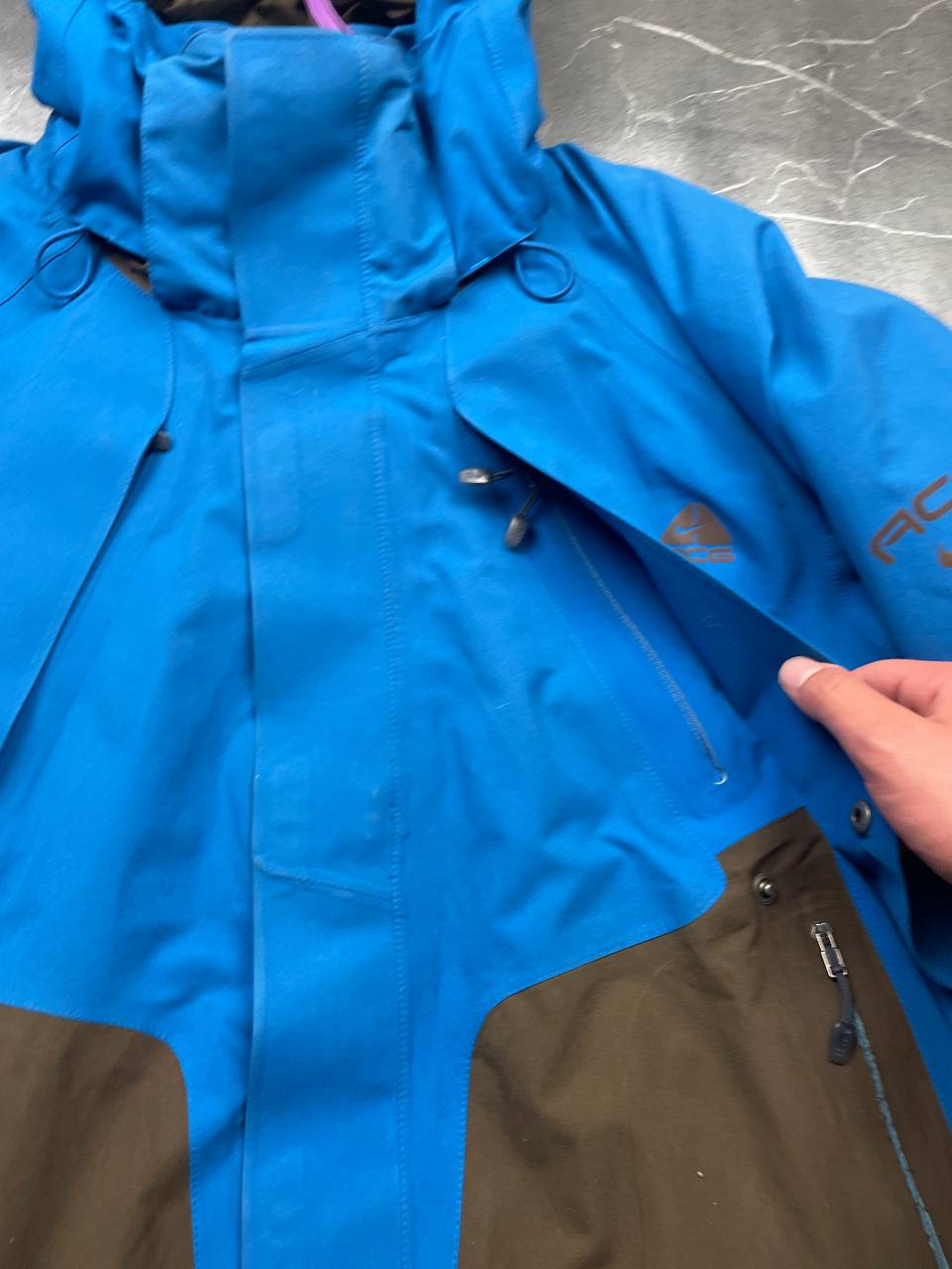 Nike ACG blue and brown waterproof jacket with Gore-Tex label and adjustable hood.