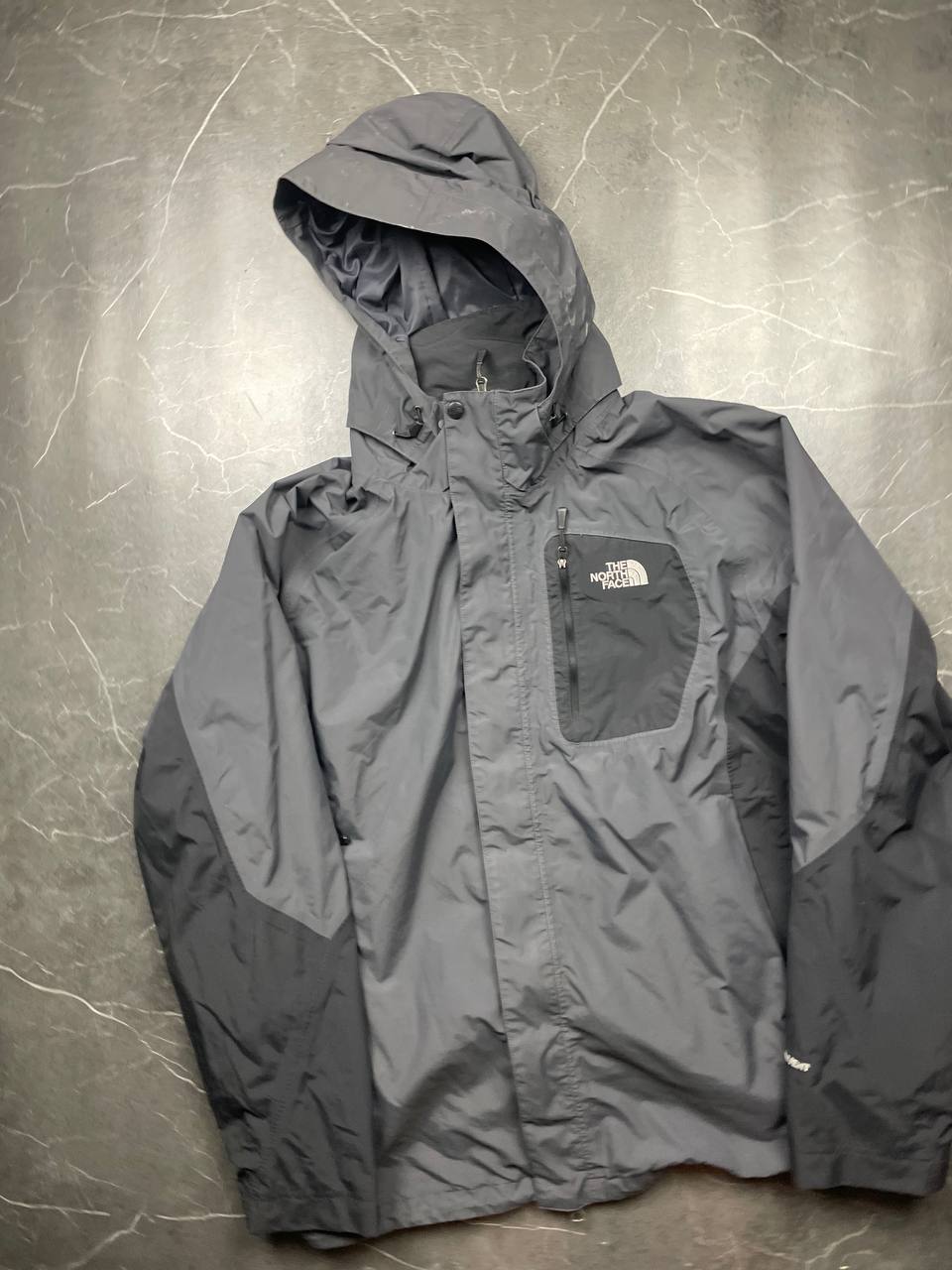The North Face black and grey waterproof jacket with hood and chest pocket.