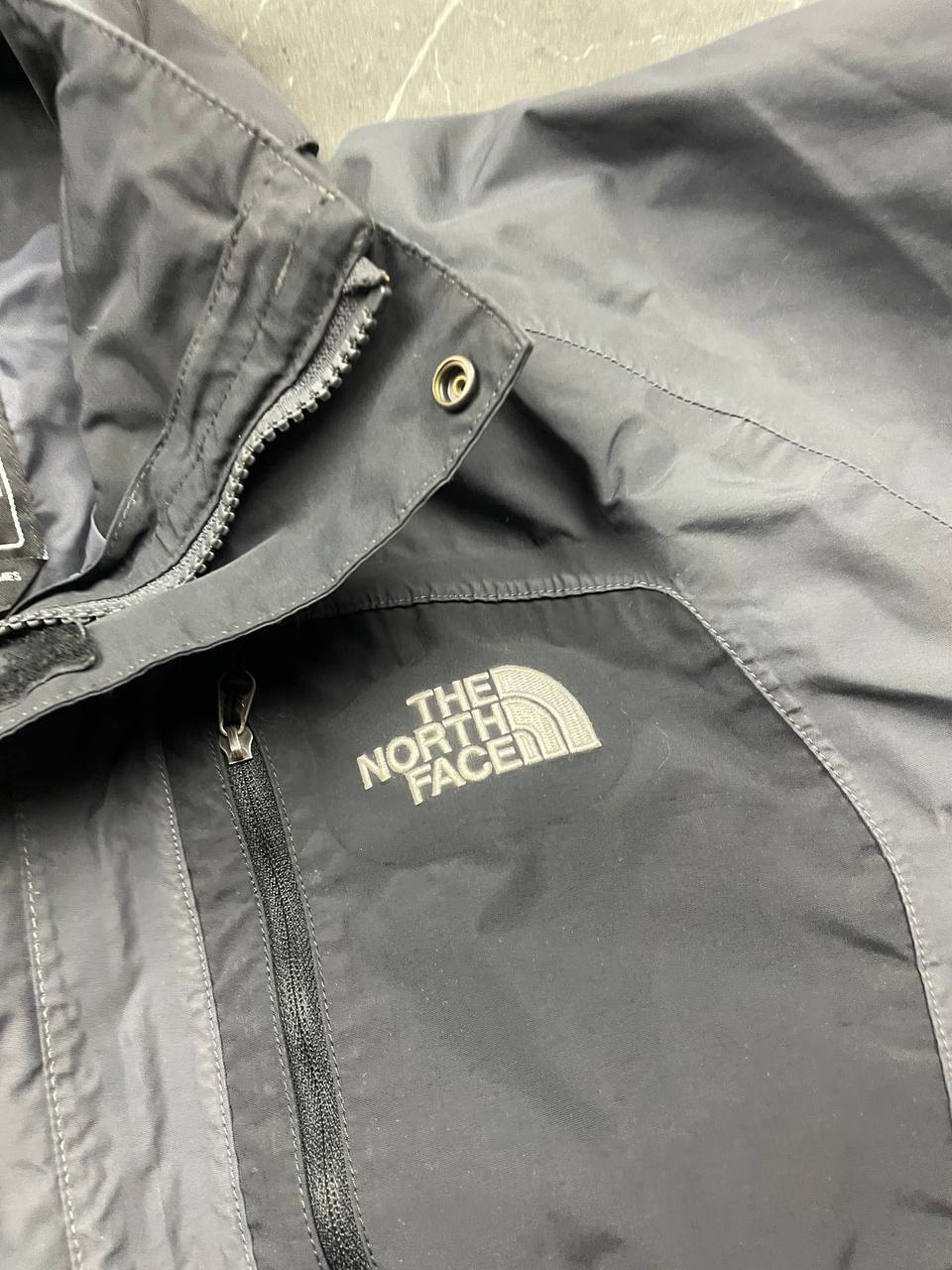 The North Face black and grey waterproof jacket with hood and chest pocket.