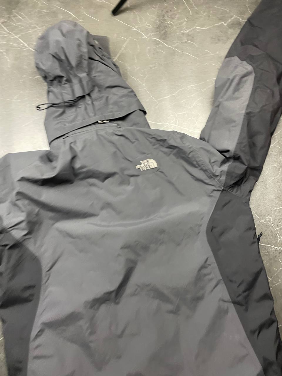 The North Face black and grey waterproof jacket with hood and chest pocket.