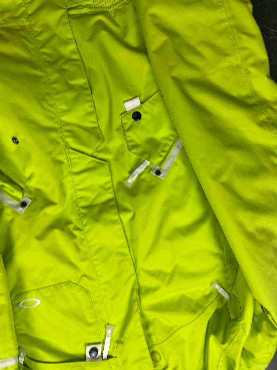 Oakley lime green ski jacket with hood, multicolored interior lining, logo on chest.