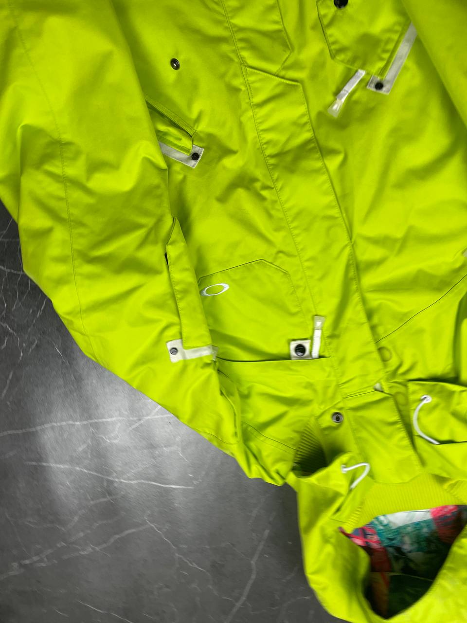 Oakley lime green ski jacket with hood, multicolored interior lining, logo on chest.