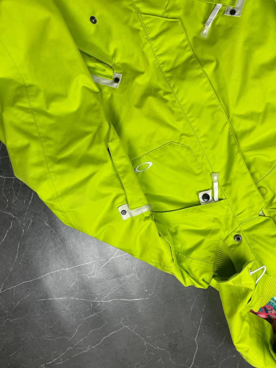 Oakley lime green ski jacket with hood, multicolored interior lining, logo on chest.