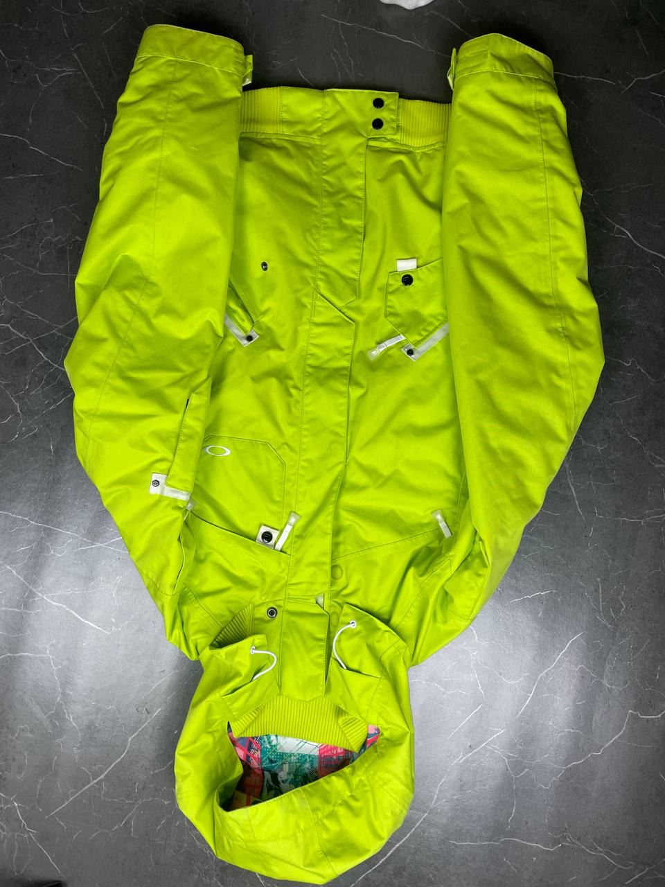 Oakley lime green ski jacket with hood, multicolored interior lining, logo on chest.