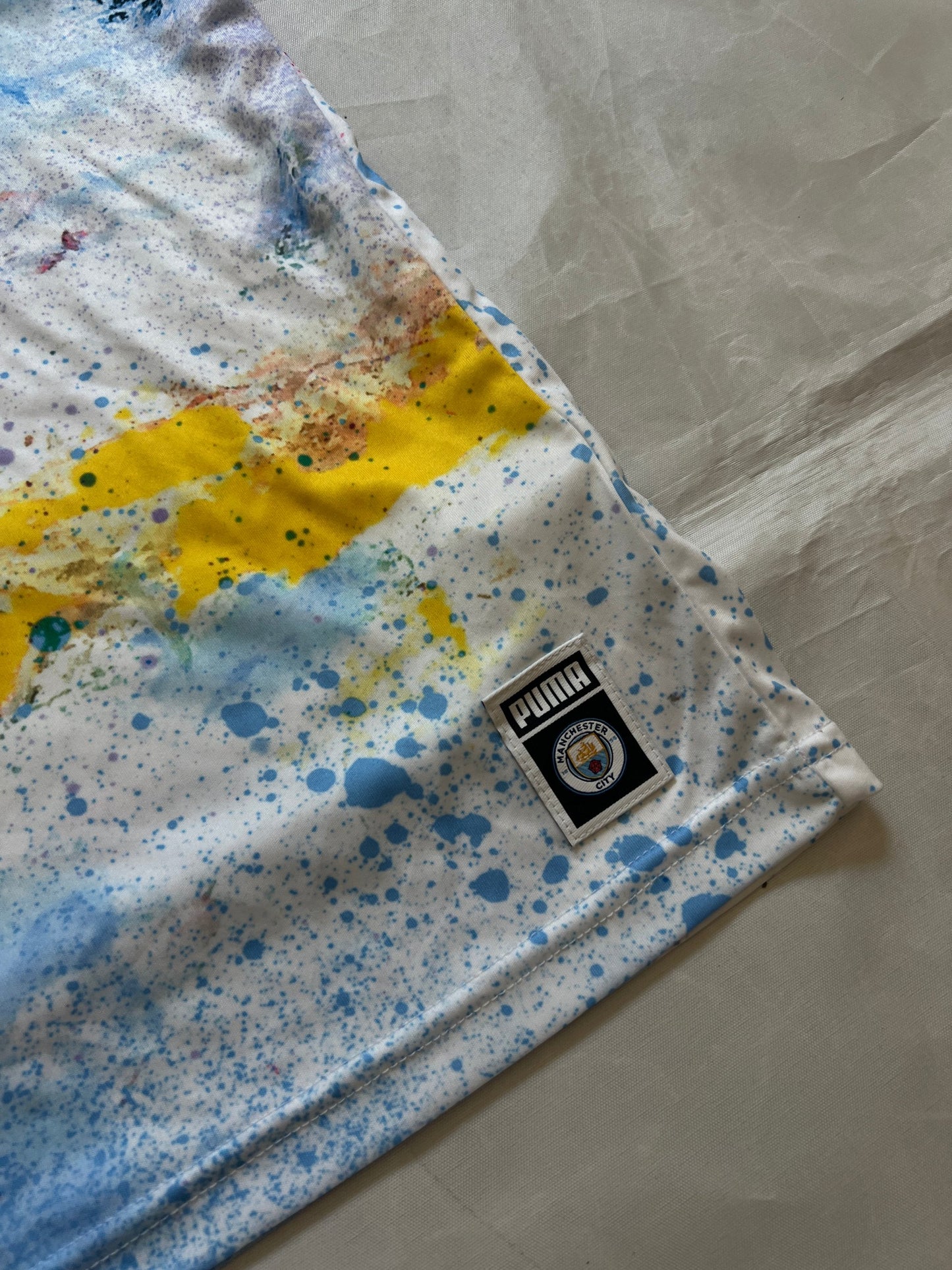 Puma blue and white football jersey with Manchester City crest and splatter paint design.