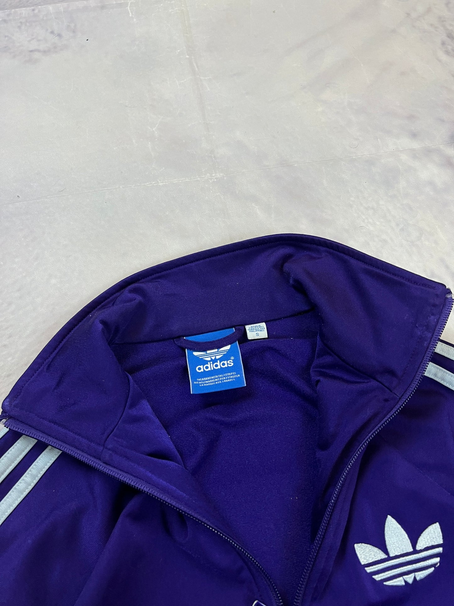 Adidas men's purple track jacket with embroidered logo and white stripes on sleeves.