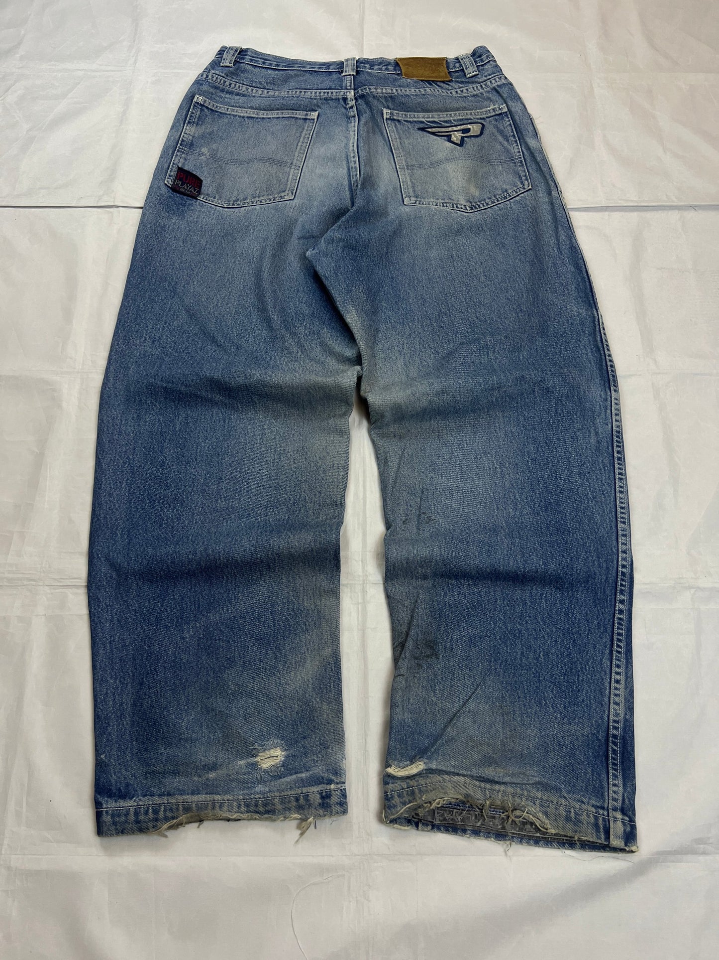 Pure Playaz blue denim jeans with distressed rips, faded wash, and branded patches.